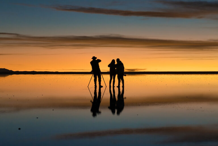 Siluetas de fotógrafos y turistas en el Salar de Uyuni al atardecer, reflejados en el espejo de agua salada
