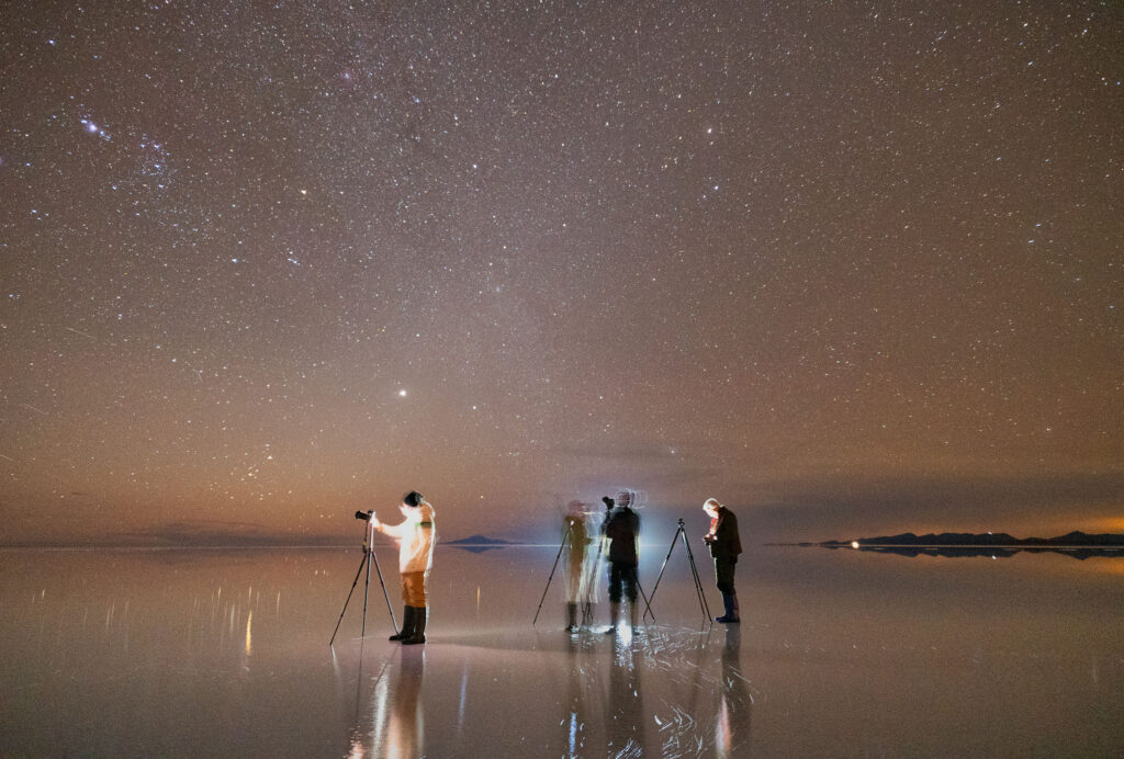 Grupo de astrofotógrafos con telescopios en el Salar de Uyuni bajo cielo estrellado y Vía Láctea