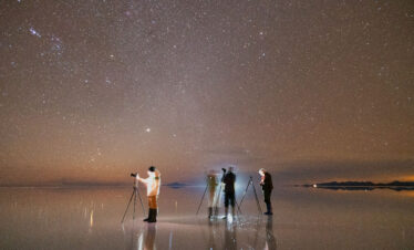 Grupo de astrofotógrafos con telescopios en el Salar de Uyuni bajo cielo estrellado y Vía Láctea