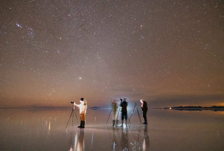 Grupo de astrofotógrafos con telescopios en el Salar de Uyuni bajo cielo estrellado y Vía Láctea