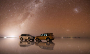 Dos vehículos 4x4 sobre el Salar de Uyuni reflejados en el espejo de agua bajo la Vía Láctea