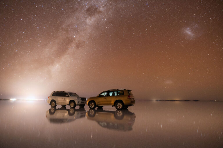 Dos vehículos 4x4 sobre el Salar de Uyuni reflejados en el espejo de agua bajo la Vía Láctea
