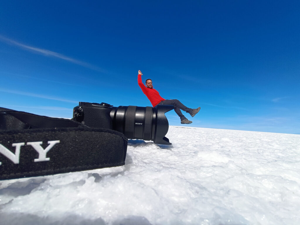 Hombre en chaqueta roja descansando sobre equipo de video en el Salar de Uyuni, desierto blanco de sal bajo cielo azul