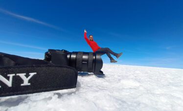 Hombre en chaqueta roja descansando sobre equipo de video en el Salar de Uyuni, desierto blanco de sal bajo cielo azul