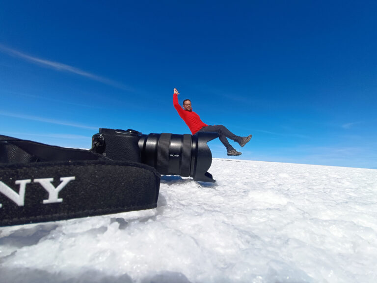Hombre en chaqueta roja descansando sobre equipo de video en el Salar de Uyuni, desierto blanco de sal bajo cielo azul