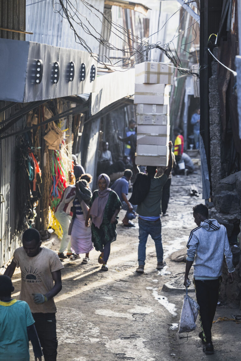 Callejón estrecho en ciudad etíope con habitantes, tiendas de artesanía y cables eléctricos entre edificios de piedra