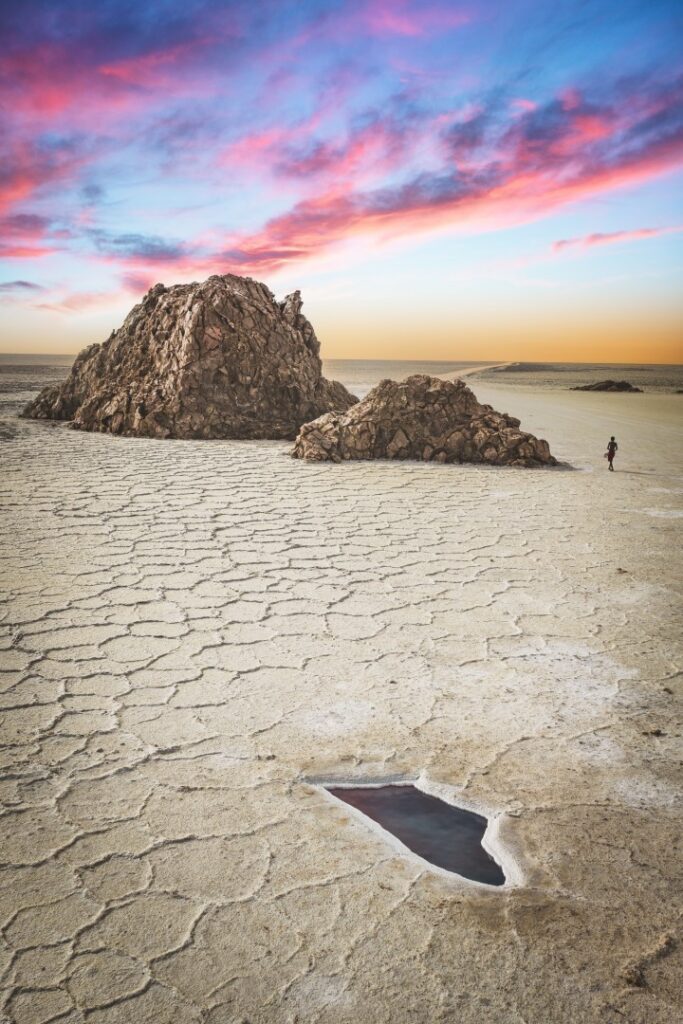 Rocas gigantes en llanura desértica con piscina mineral y atardecer rosado en el horizonte