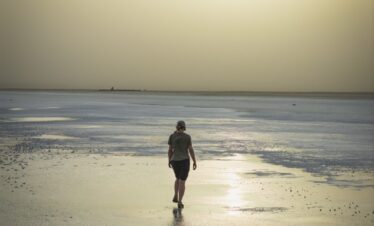 Corredor solitario en playa de arena húmeda al atardecer con aguas tranquilas al fondo