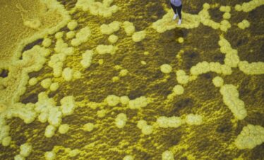 Persona con brazos extendidos sobre formaciones geológicas amarillas y verdes en paisaje desértico visto desde arriba