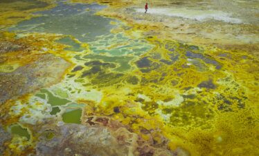 Termas geotérmicas con aguas minerales amarillas y verdes en Etiopía, con un explorador caminando entre fumarolas