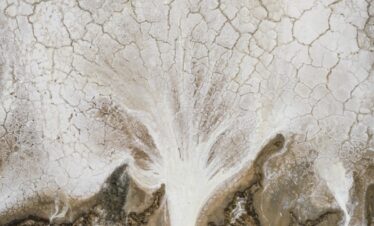 Vista aérea de río sinuoso atravesando llanura desértica con grietas de sequía en tierra blanca y árida