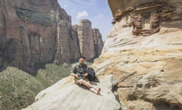 Expedicionario sentado en roca con acantilados de piedra al fondo en Etiopía