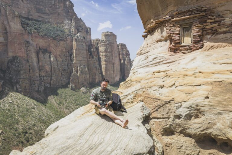Expedicionario sentado en roca con acantilados de piedra al fondo en Etiopía