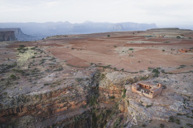 Construcción de piedra sobre acantilado en meseta etíope con montañas al fondo y paisaje árido