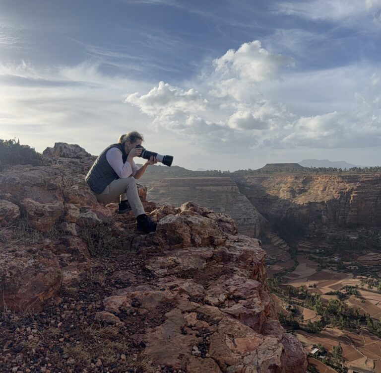Fotógrafo con teleobjetivo en acantilado rocoso capturando el paisaje de cañones y valles de Etiopía