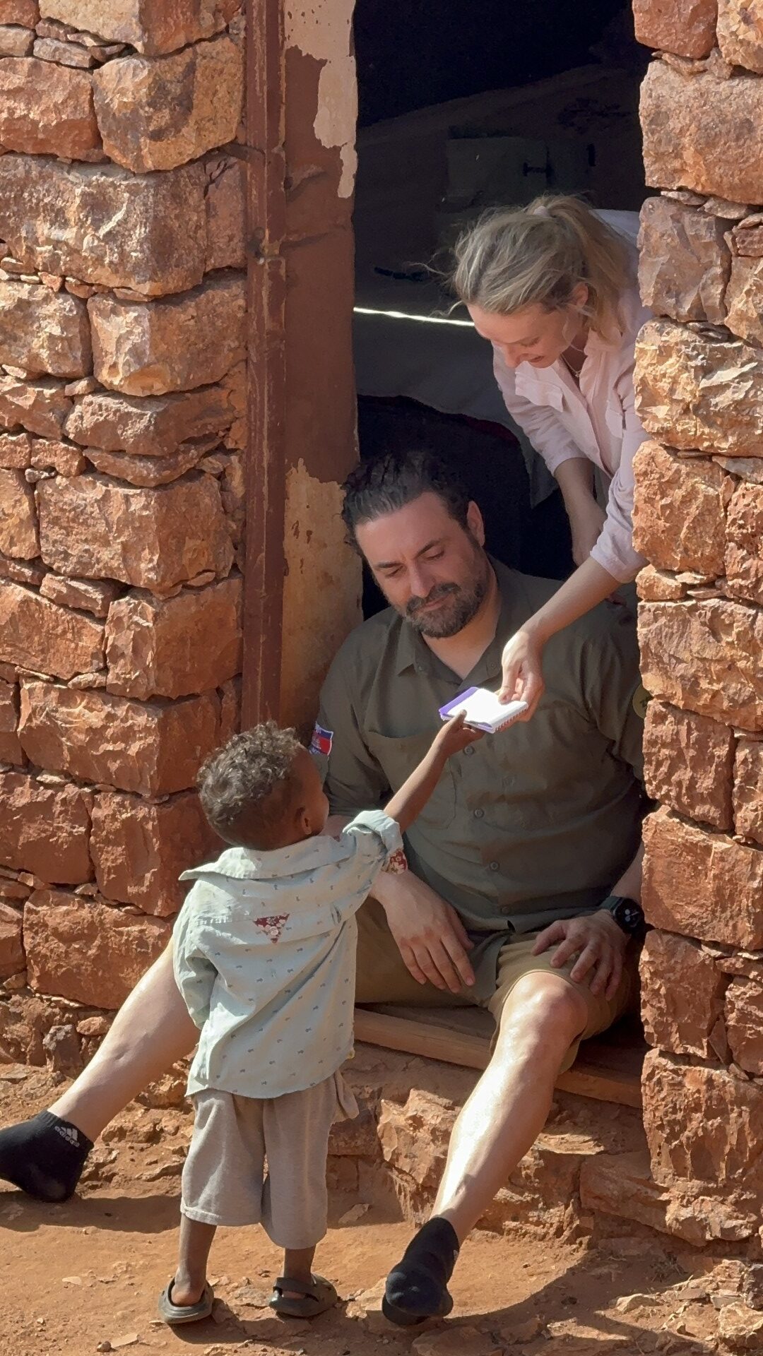 Guía mostrando dispositivo móvil a niño etíope en entrada de construcción de piedra roja