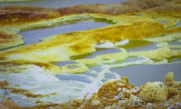 Piscinas termales de aguas azules rodeadas de depósitos minerales amarillos y blancos en el desierto etíope