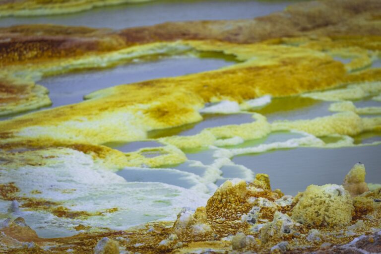 Piscinas termales de aguas azules rodeadas de depósitos minerales amarillos y blancos en el desierto etíope