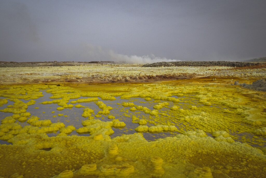 Aguas termales amarillentas con depósitos minerales en paisaje volcánico de Etiopía