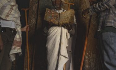 Sacerdote etíope con turbante blanco sostiene libro sagrado en iglesia antigua decorada con iconografía religiosa