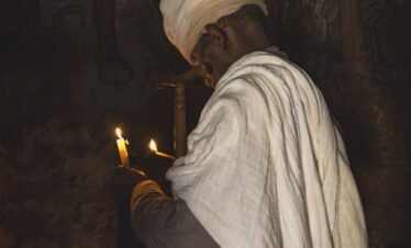 Peregrino etíope con túnica blanca sostiene velas encendidas frente a relieves antiguos en templo