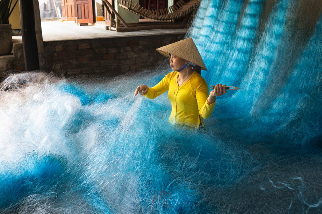 Mujer vietnamita en áo dài amarillo tejiendo red azul en el Delta del Mekong