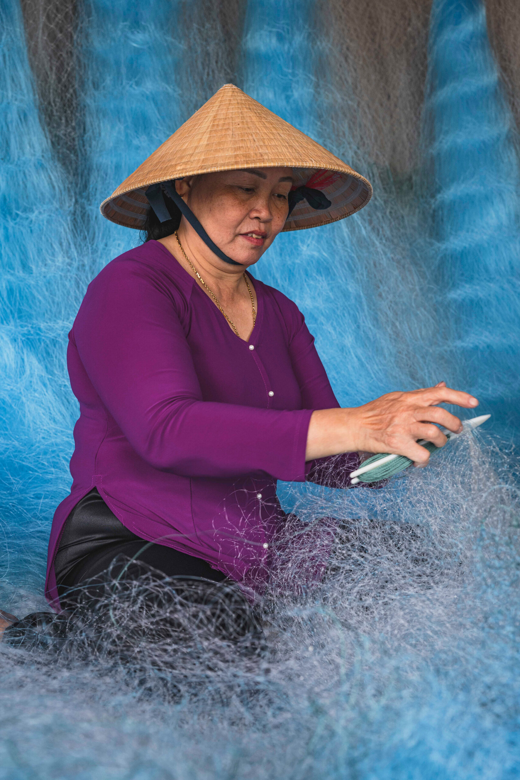 Mujer vietnamita con sombrero cónico tejiendo redes de pesca en el Delta del Mekong