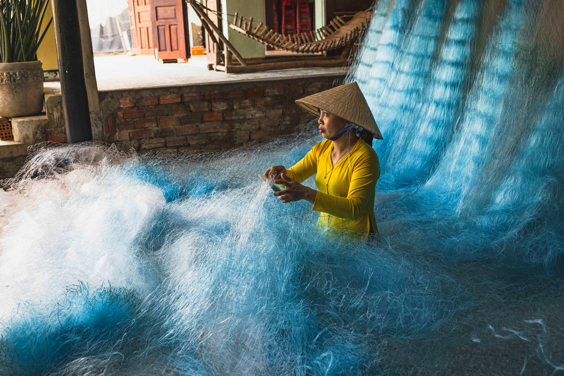 Artesana vietnamita en amarillo teje redes azules en el Delta del Mekong