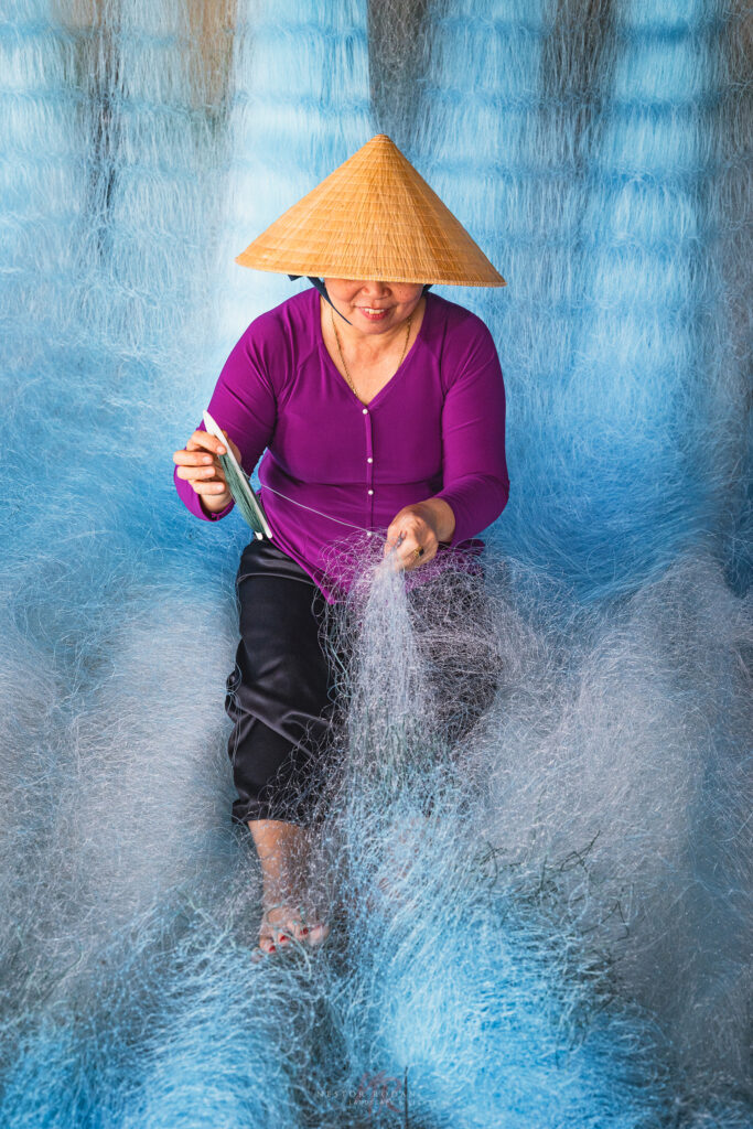 Mujer vietnamita con cono tradicional tejiendo red de pesca en el agua del Delta del Mekong