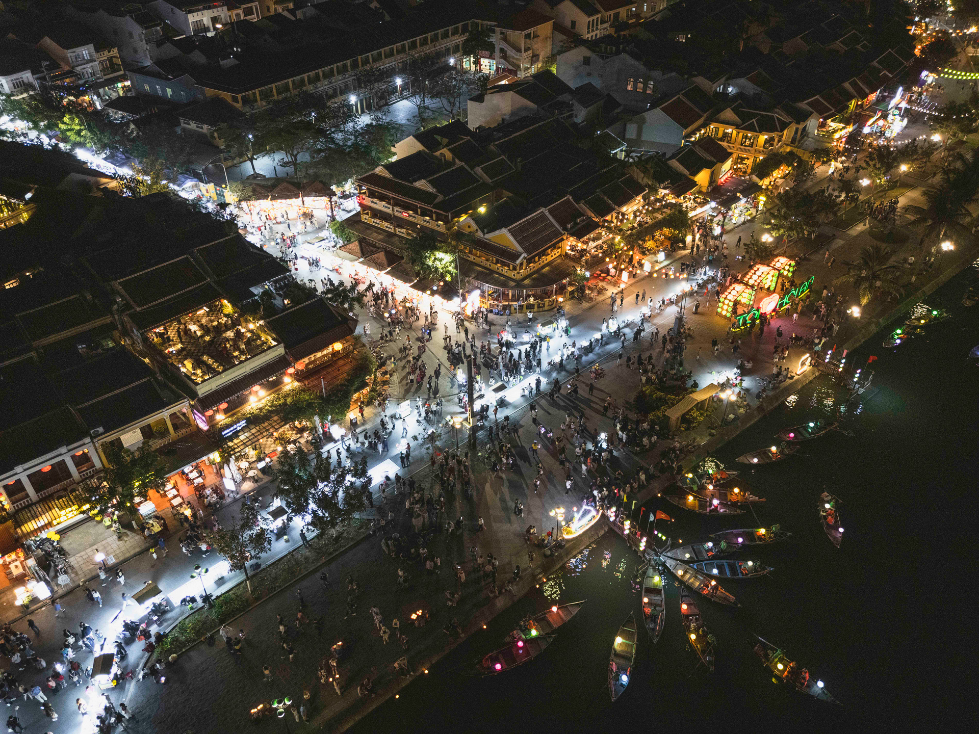 Vista aérea nocturna de mercado flotante iluminado en Vietnam con embarcaciones, tiendas y multitud de visitantes