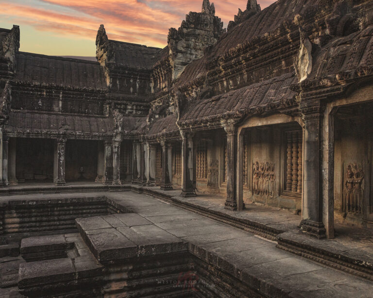 Claustro interior de Angkor Wat con columnas de piedra, relieves tallados y estanque reflectante al atardecer