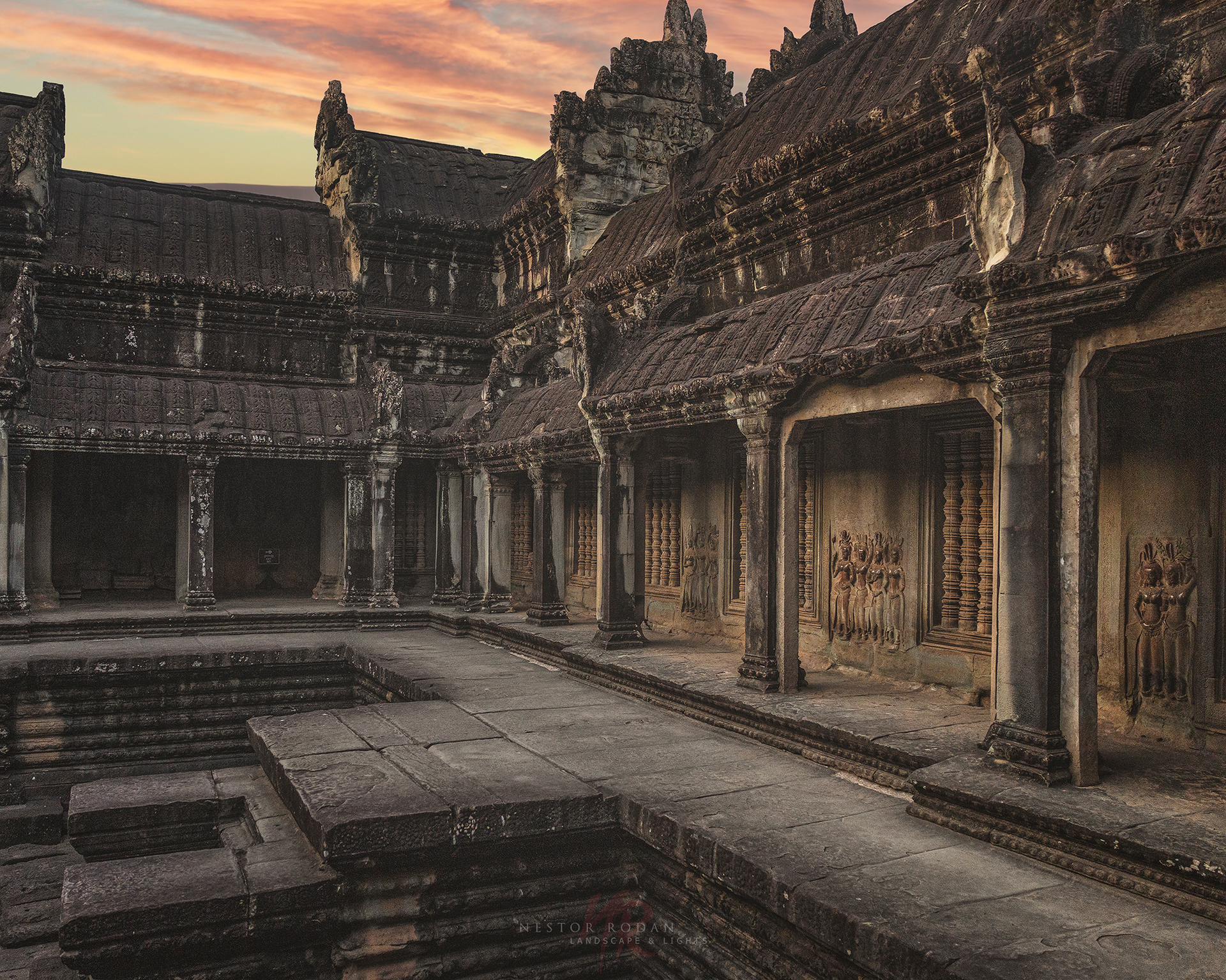 Claustro interior de Angkor Wat con columnas de piedra, relieves tallados y estanque reflectante al atardecer