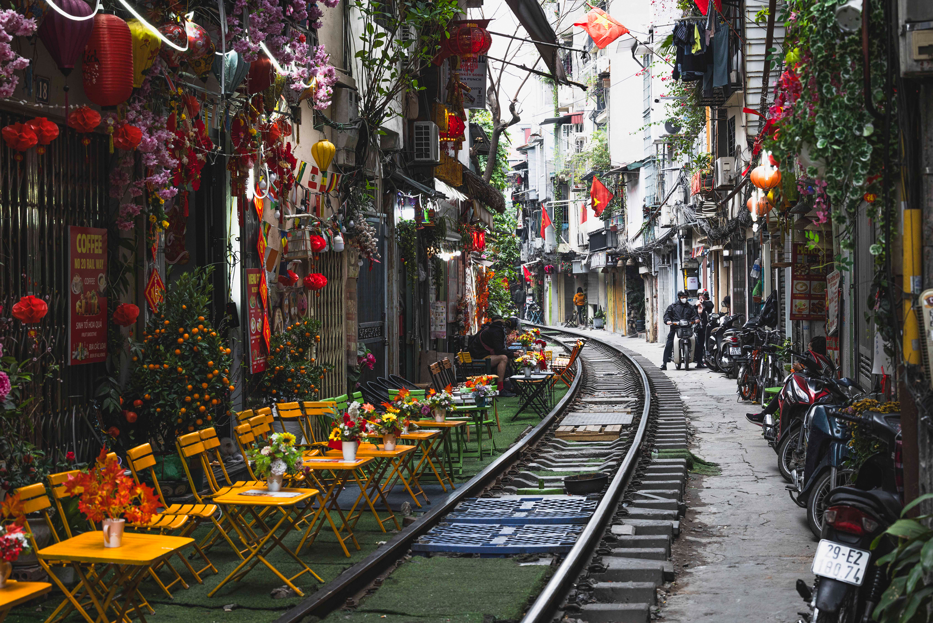 Calle de vía ferroviaria en Hanói decorada con flores de papel rojo, mesas amarillas y bicicletas aparcadas a ambos lados