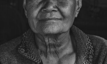 Retrato en blanco y negro de un hombre mayor camboyano con expresión serena, vistiendo chaqueta tradicional con bordados