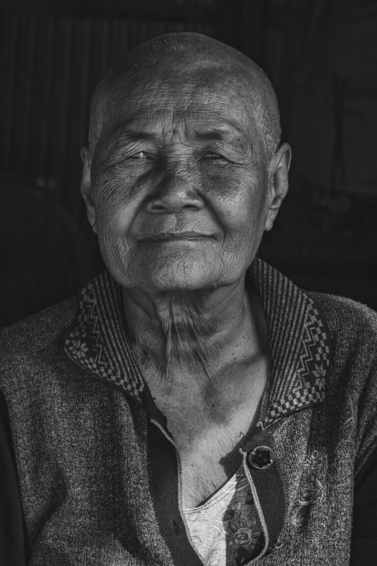 Retrato en blanco y negro de un hombre mayor camboyano con expresión serena, vistiendo chaqueta tradicional con bordados