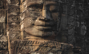 Rostro tallado en piedra de un templo antiguo en Camboya, con ornamentación decorativa y detalles arquitectónicos erosionados