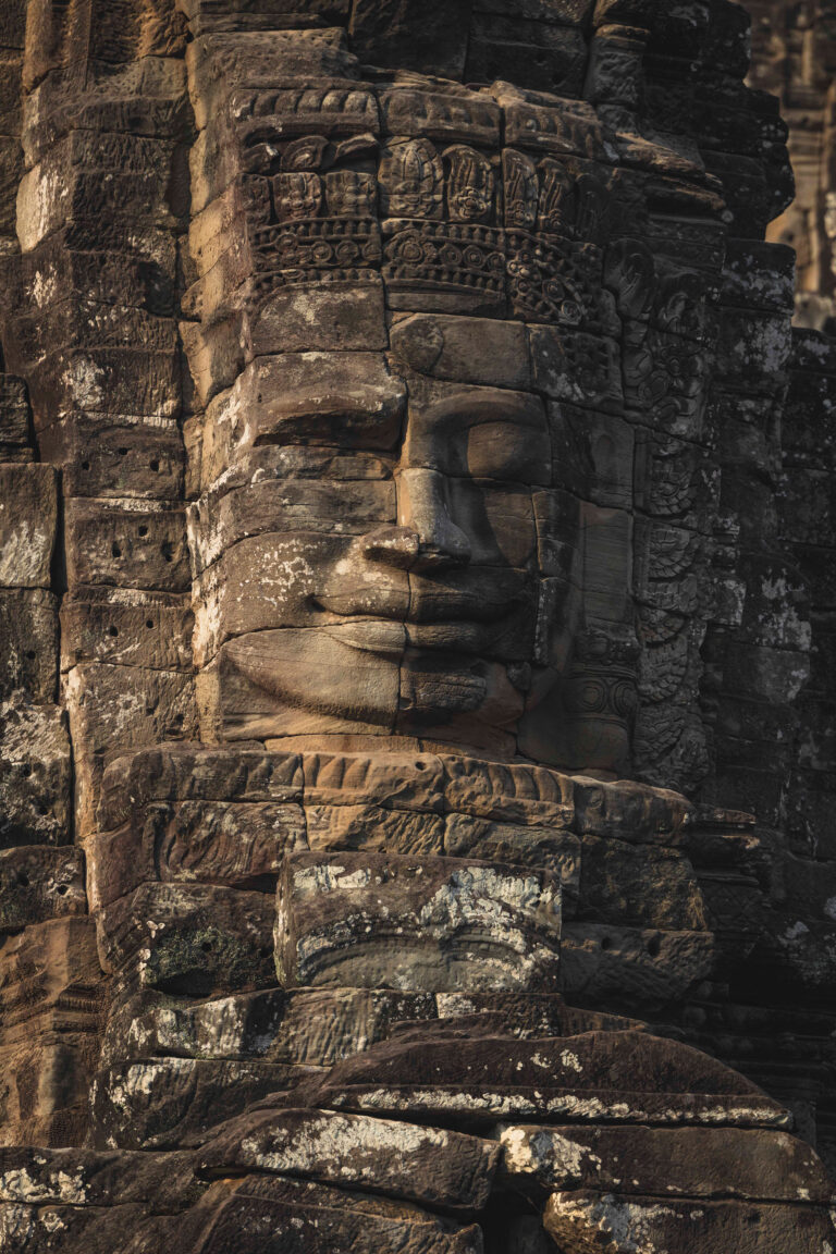 Rostro tallado en piedra de un templo antiguo en Camboya, con ornamentación decorativa y detalles arquitectónicos erosionados