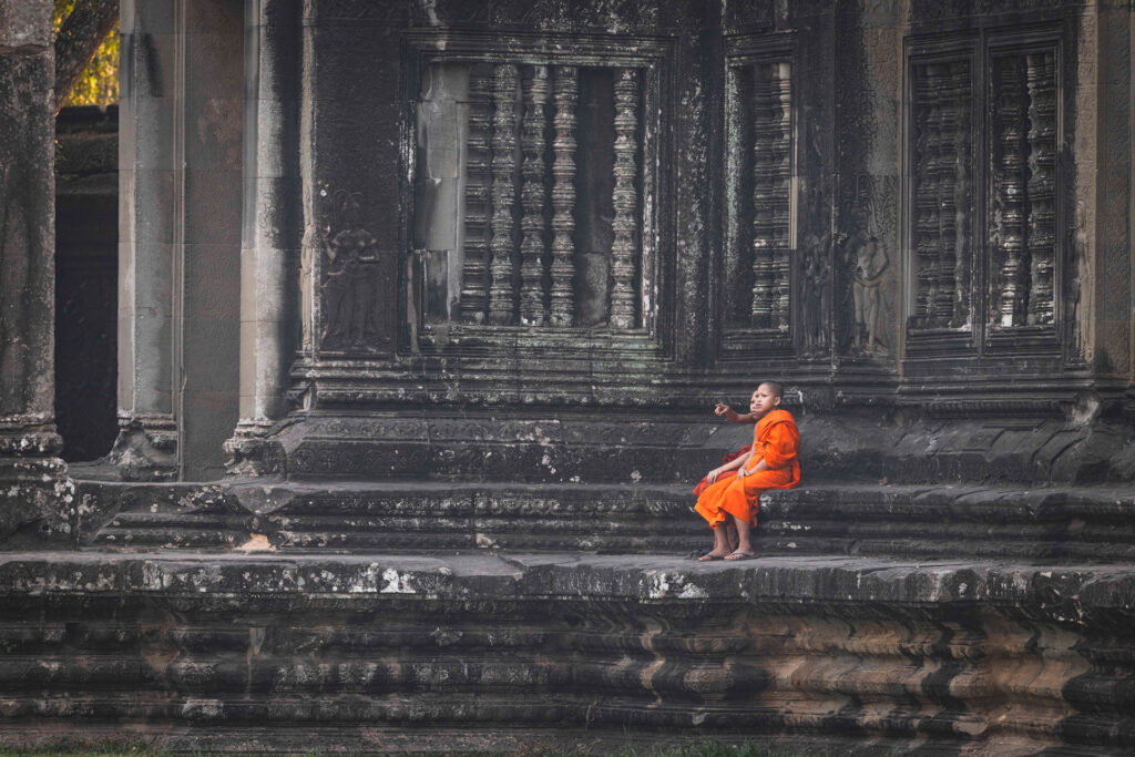 Monje budista en túnica naranja sentado en escalones de templo de piedra antigua en Camboya
