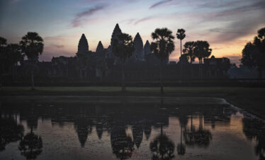 Templo de Angkor Wat reflejado en el agua al atardecer con palmeras y cielo rosado