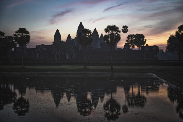Templo de Angkor Wat reflejado en el agua al atardecer con palmeras y cielo rosado