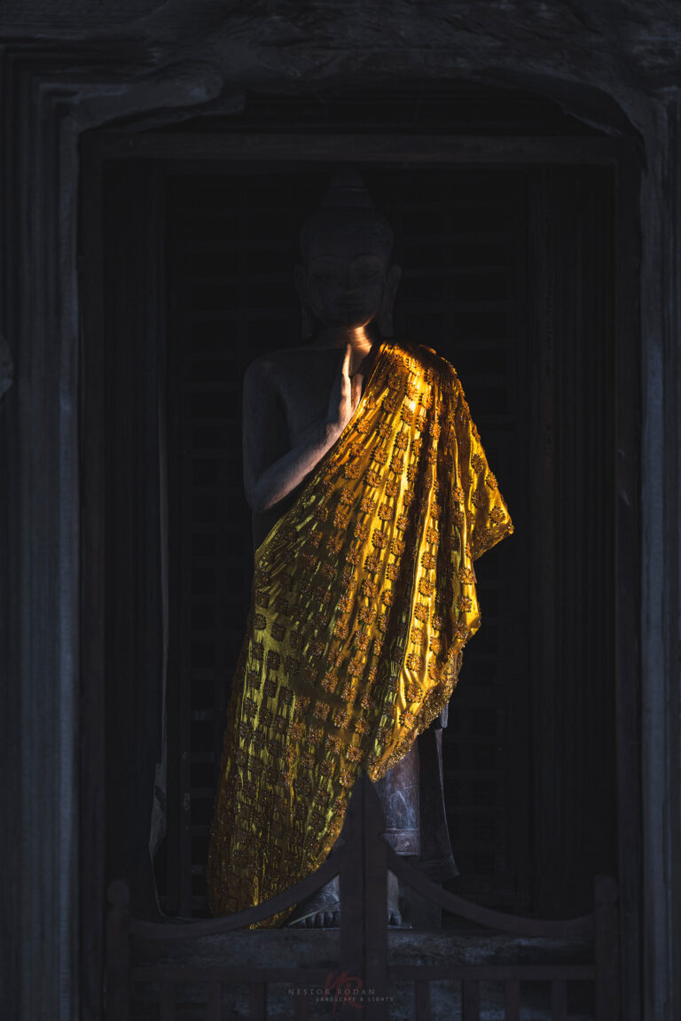 Monje budista con túnica dorada en el interior oscuro de un templo de Camboya
