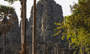 Templo antiguo de piedra en Camboya rodeado de árboles tropicales y palmeras, con torres de arquitectura jemer al fondo