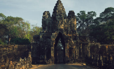 Puerta de piedra antigua con torres en ruinas, rodeada de vegetación tropical y árboles frondosos