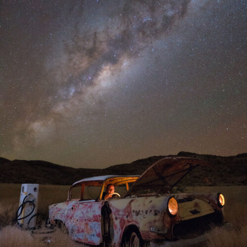 Coche abandonado oxidado en el desierto de Namibia bajo la Vía Láctea con persona iluminada en el interior