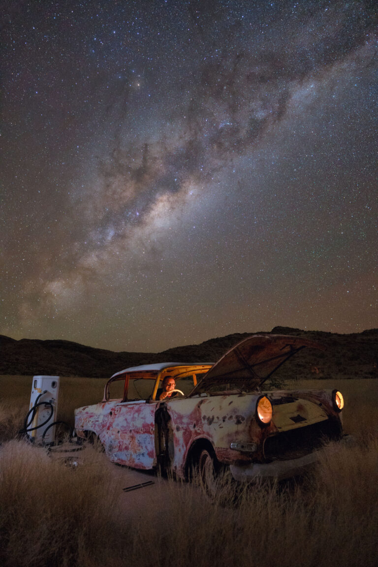 Coche abandonado oxidado en el desierto de Namibia bajo la Vía Láctea con persona iluminada en el interior