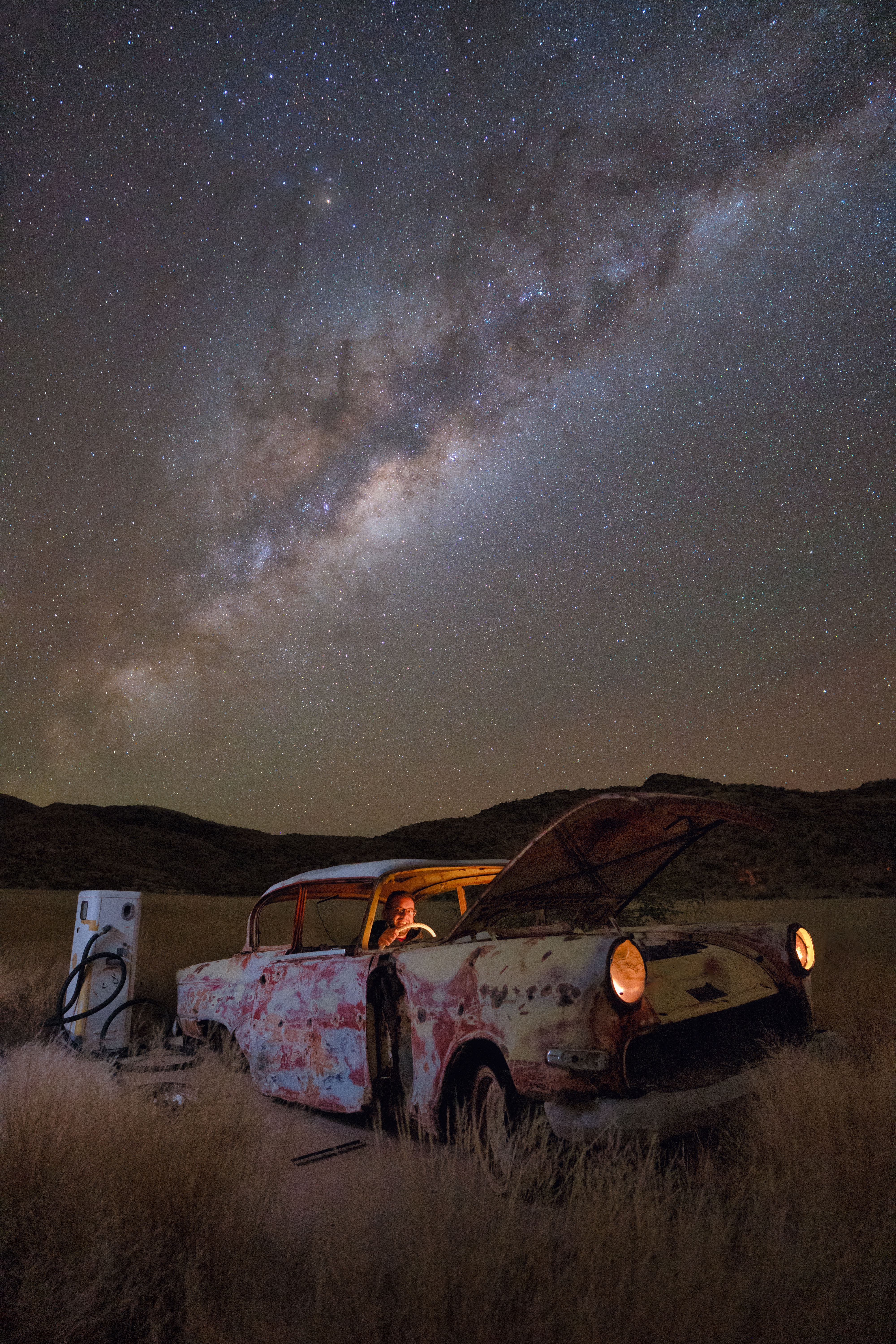 Coche abandonado oxidado en el desierto de Namibia bajo la Vía Láctea con persona iluminada en el interior