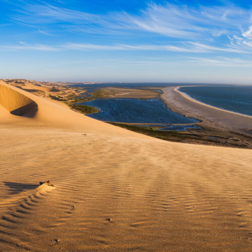 Dunas de arena dorada junto a laguna azul y playa con océano al fondo en Namibia