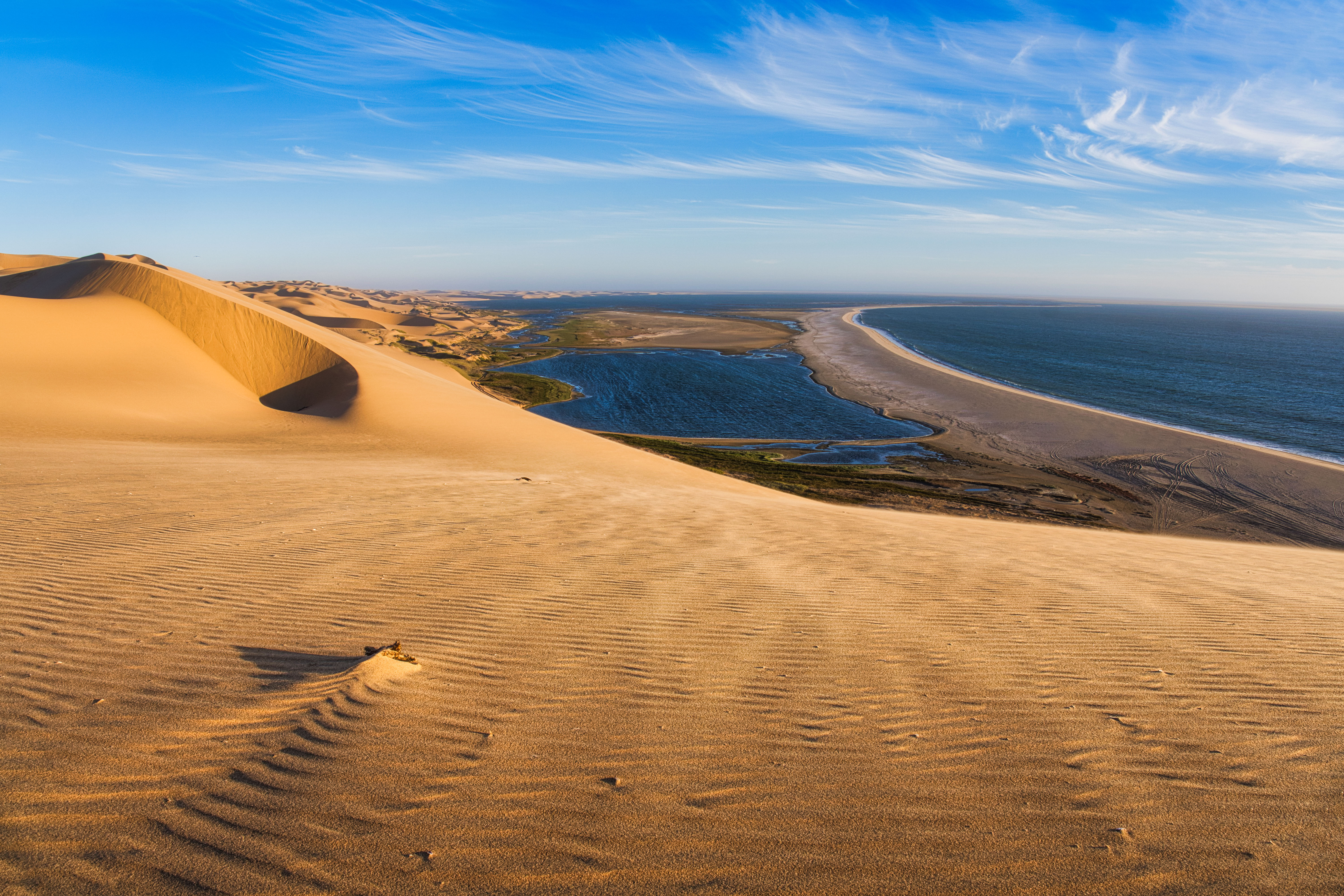 Dunas de arena dorada junto a laguna azul y playa con océano al fondo en Namibia