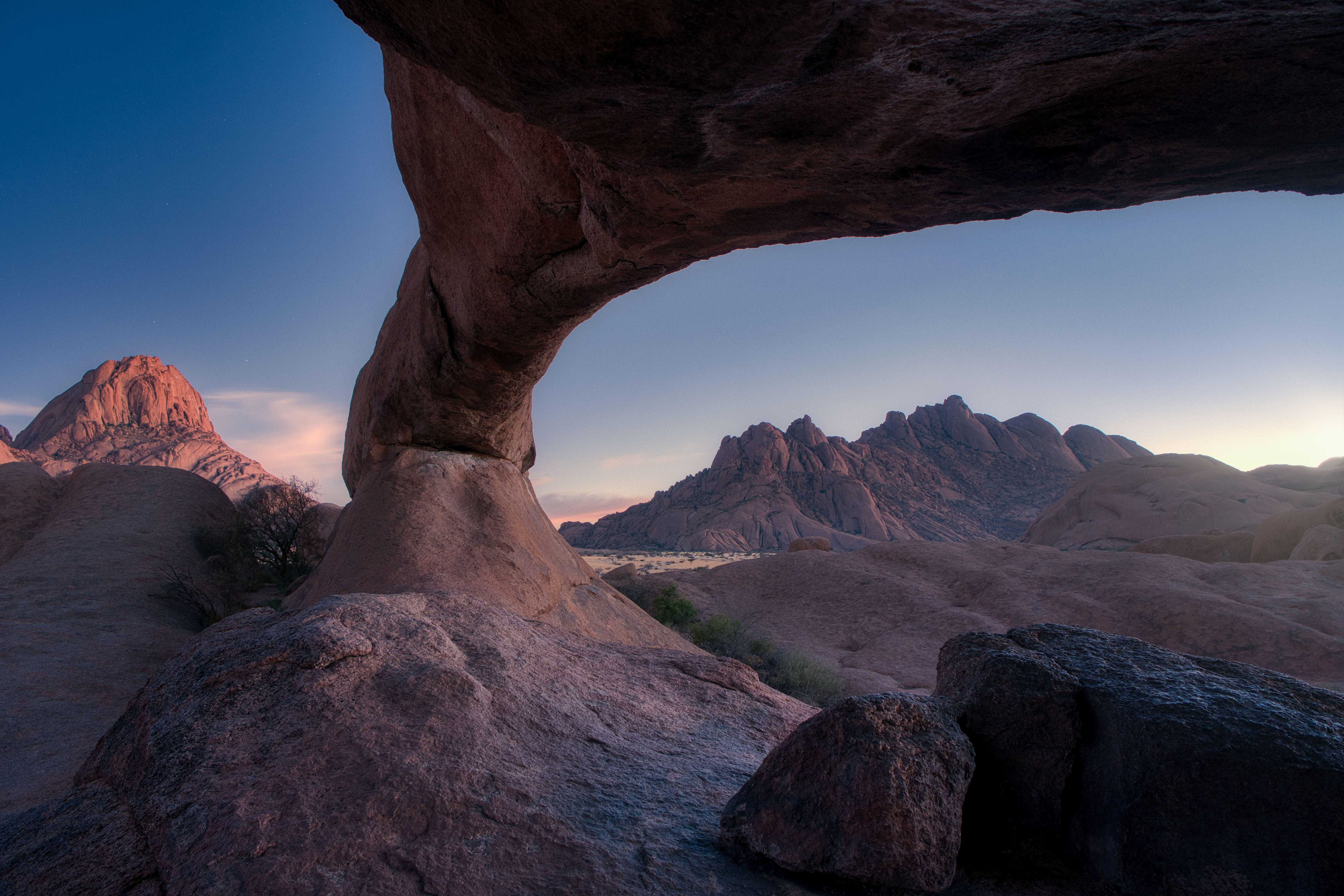 Formación rocosa con arco natural enmarcando montañas desérticas al atardecer en Namibia