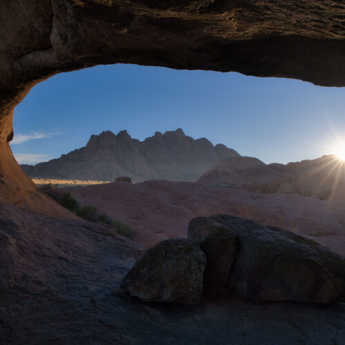 Arco de roca natural enmarcando montaña rocosa al atardecer en desierto de Namibia